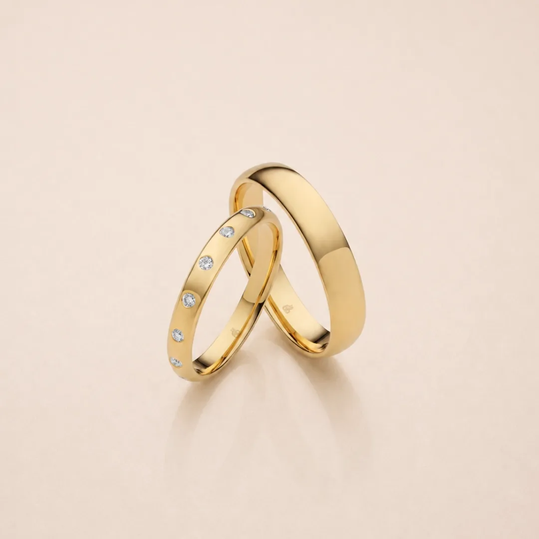 A matched pair of RAUSCHMAYER wedding bands in yellow gold, one diamond-set and one plain